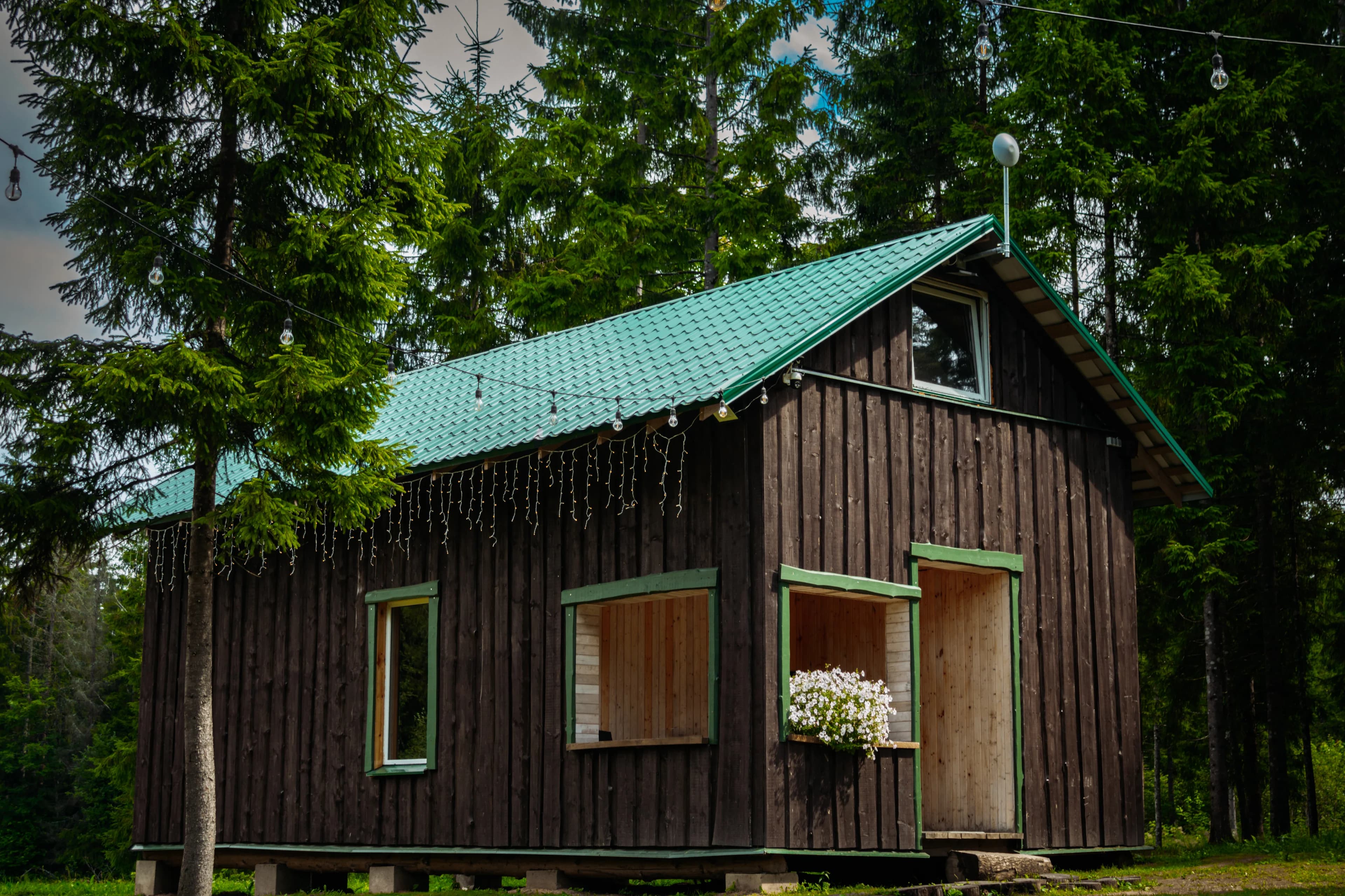 Lielā namiņa fasāde ar gala logu un puķu kastēm vasarā